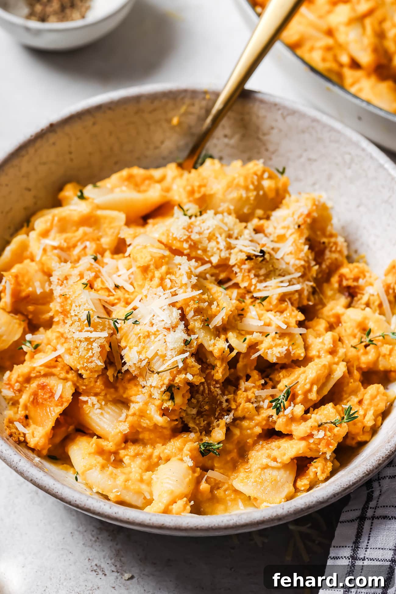 A close-up shot of a single serving of butternut squash mac and cheese in a white bowl, a golden spoon resting in its creamy depths.