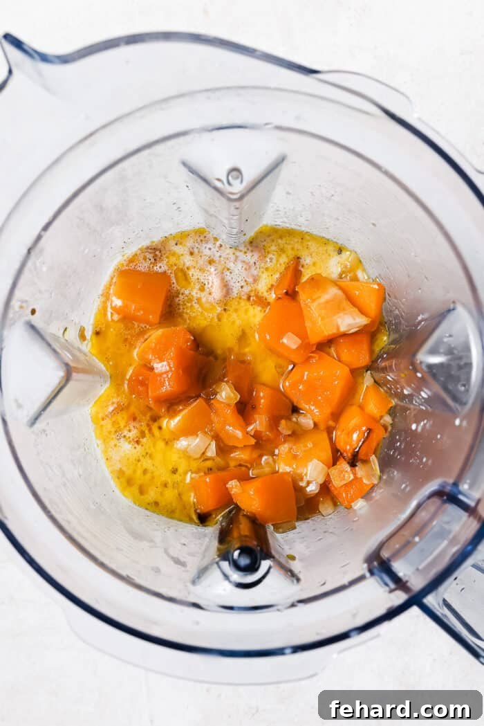 Roasted butternut squash, shallots, garlic, and spices placed inside a blender, ready to be transformed into a smooth sauce.