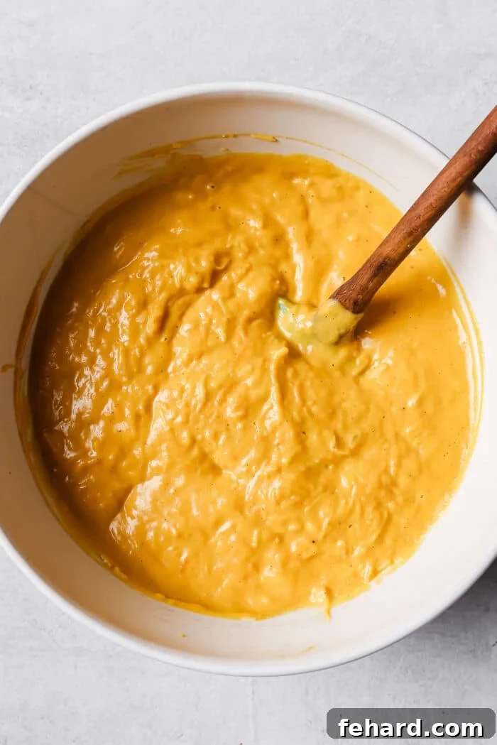 A rich, golden butternut squash sauce resting in a white bowl, ready for the addition of grated cheeses.