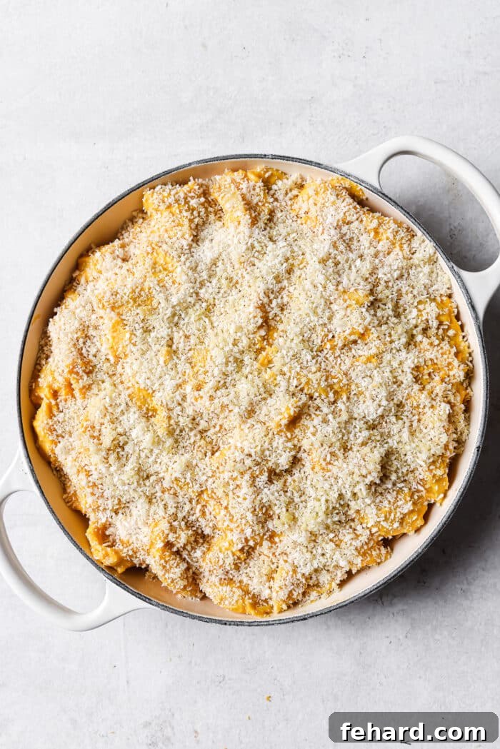 Unbaked butternut squash mac and cheese, perfectly mixed and smoothed into a white skillet, awaiting its crispy breadcrumb topping.