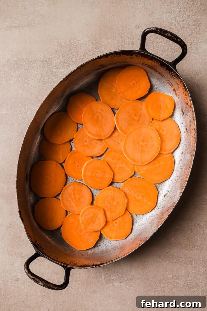Golden Sweet Potato Bake 5 An overhead view of thinly sliced sweet potatoes arranged in a single, even layer in a greased baking pan.