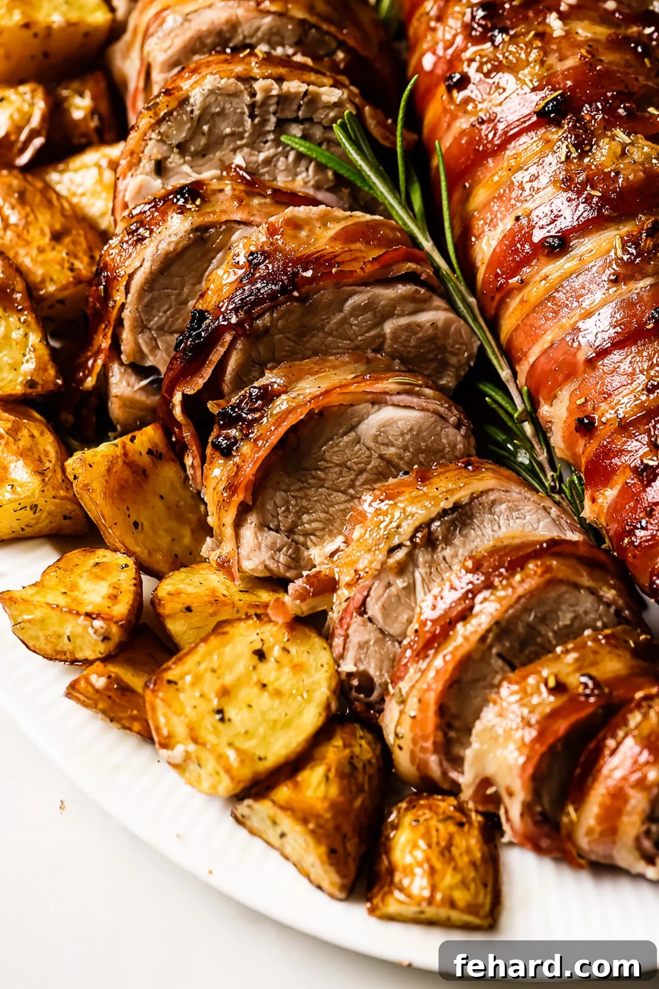 Sliced pork tenderloin on a serving dish with roasted potatoes on the side. 