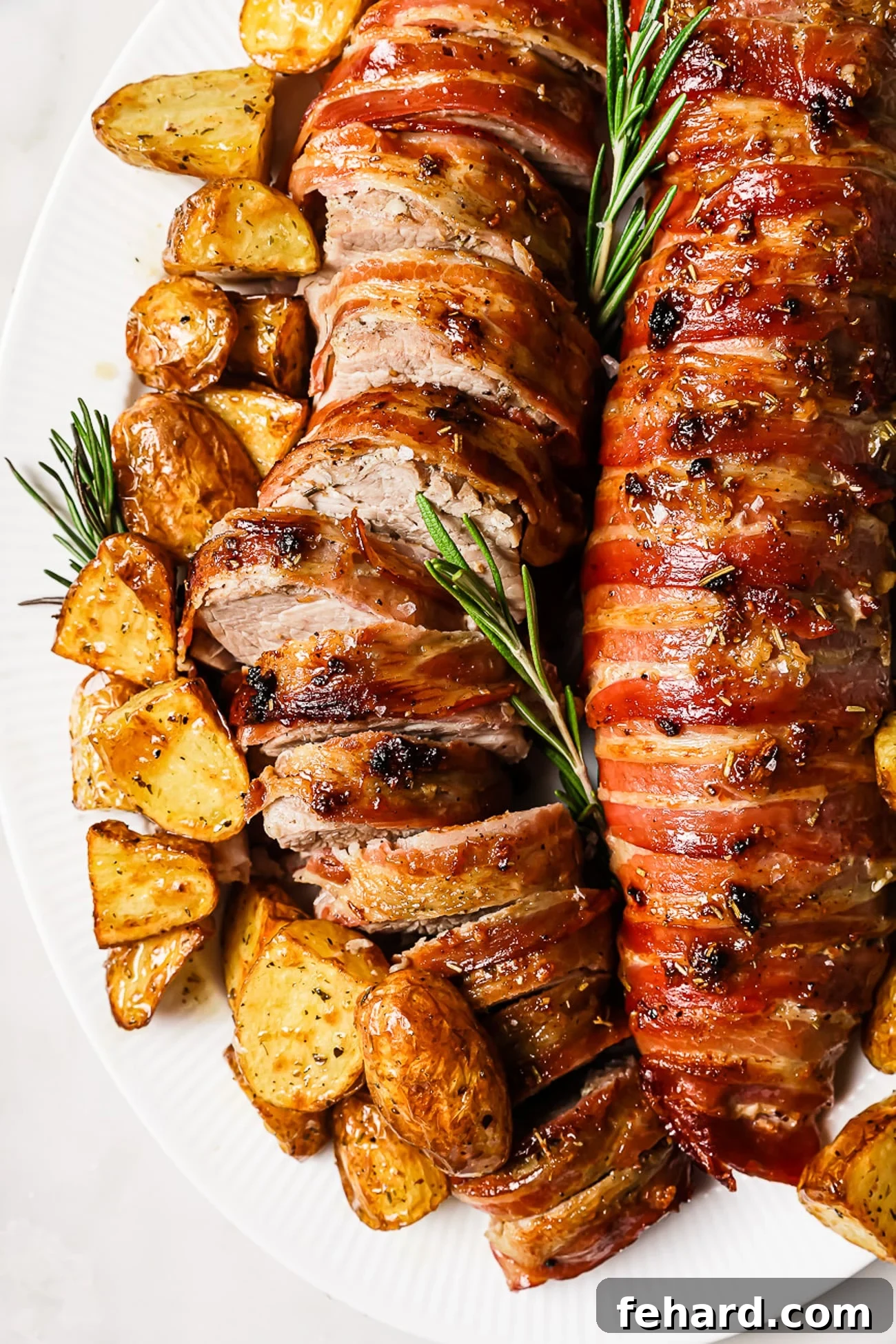 An overhead view of bacon-wrapped pork tenderloin with roasted potatoes. 