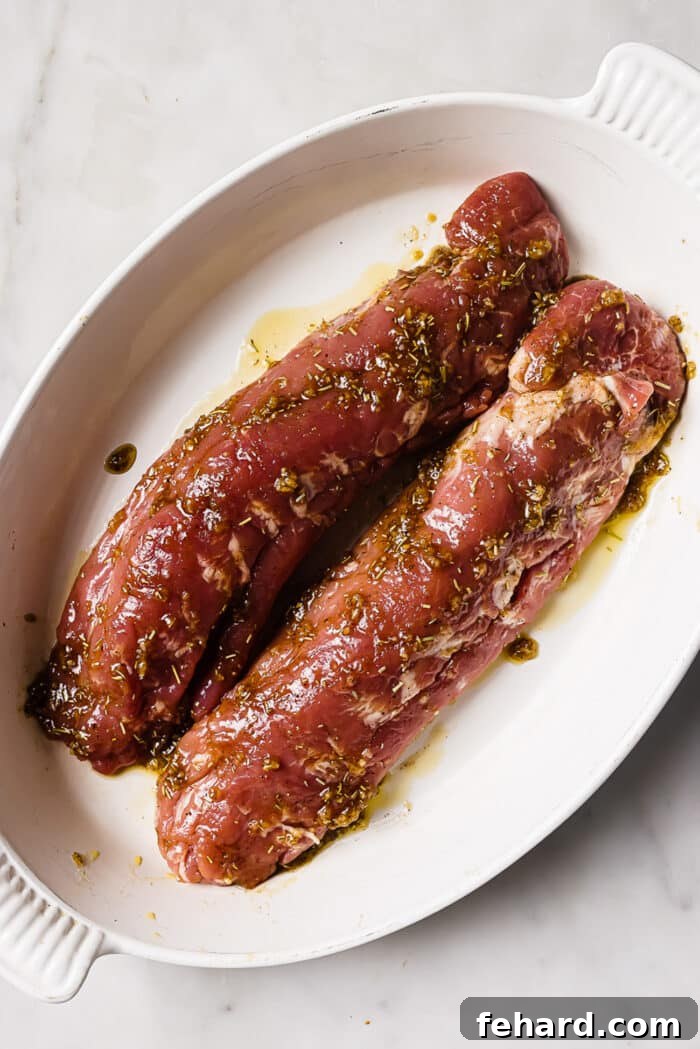 Two seasoned pork tenderloins in a white roasting dish. 