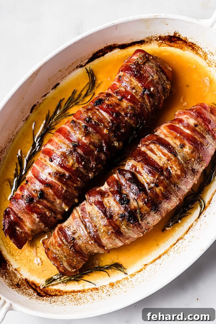 An overhead view of two roasted pork tenderloins wrapped in back. 
