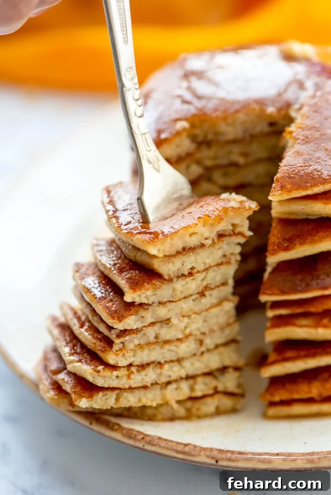 A beautifully stacked plate of banana oatmeal pancakes with a triangular bite taken out, showcasing their light and airy texture. Ready to be enjoyed for a healthy breakfast.