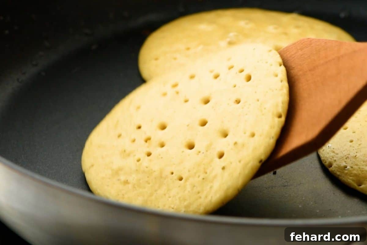 A spatula flipping an oatmeal pancake on a skillet after small bubbles have formed on the surface, indicating it's ready.