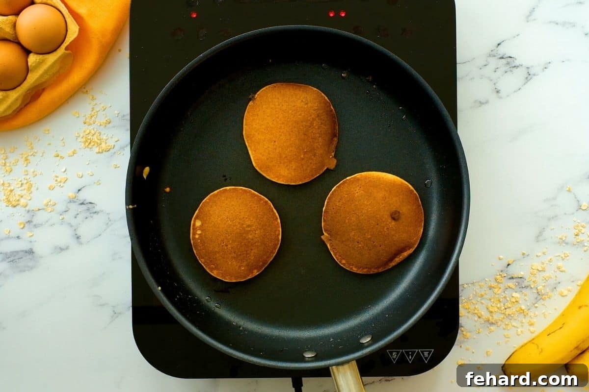 Golden-brown banana oatmeal pancakes resting in a skillet after being perfectly cooked, showing their appealing texture.