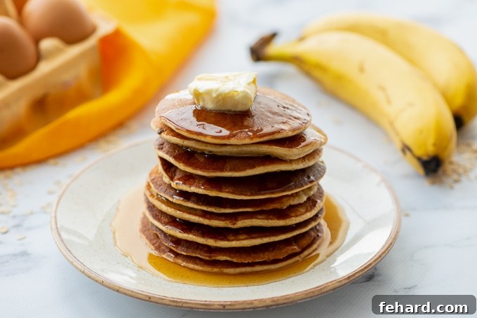 A inviting stack of Blender Oat Pancakes on a plate, garnished with fresh banana slices and a light drizzle, with more bananas in the background.