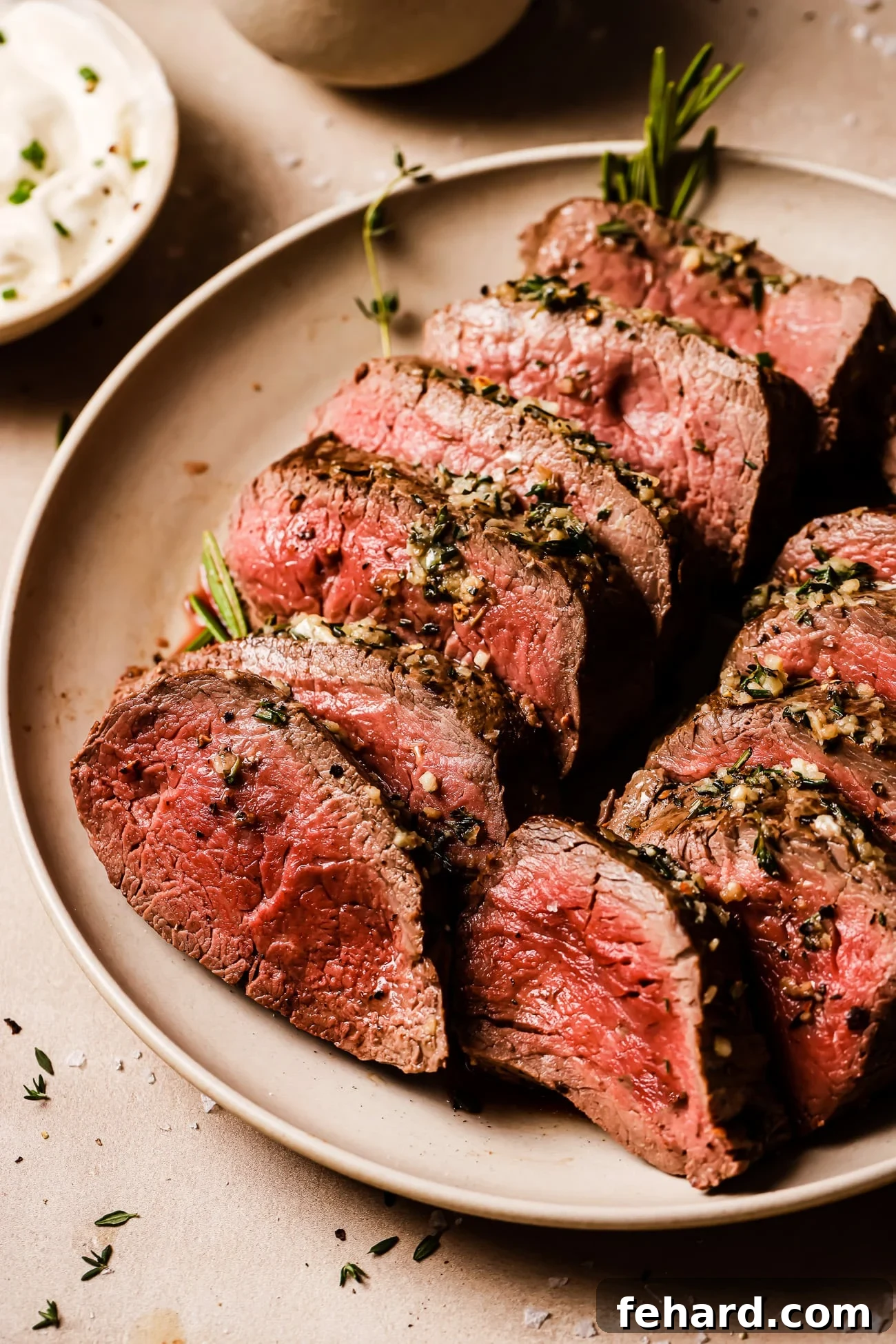 Golden Garlic Butter Tenderloin 2 Sliced garlic butter beef tenderloin garnished with rosemary on a serving platter.