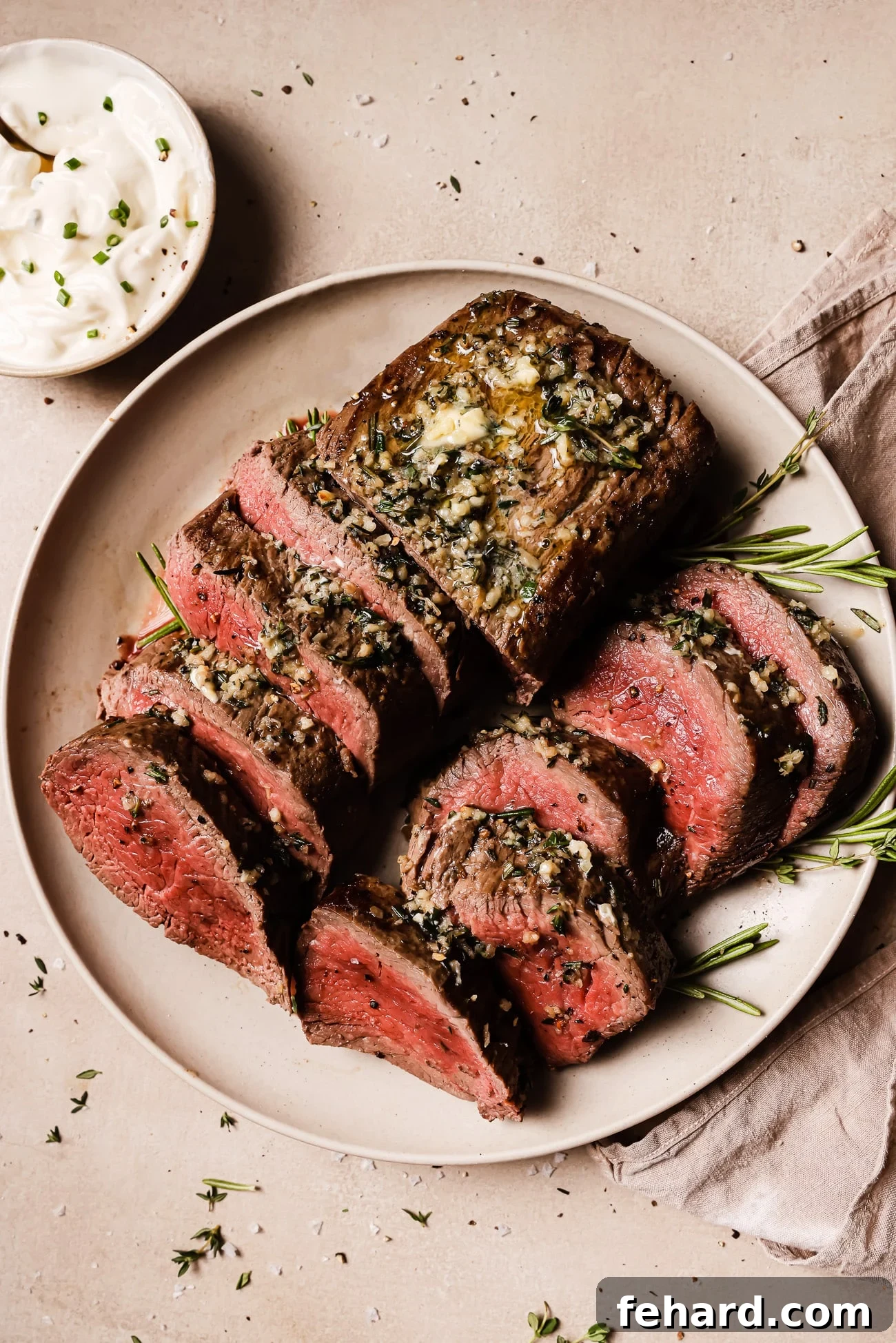 Golden Garlic Butter Tenderloin 11 An overhead view of two beef tenderloins sliced on a white serving plate.