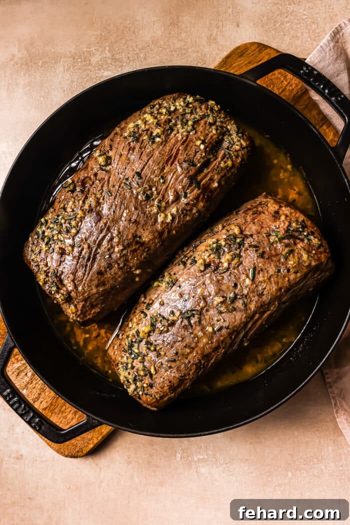 Golden Garlic Butter Tenderloin 8 Two cooked garlic butter beef tenderloins in a cast iron skillet.