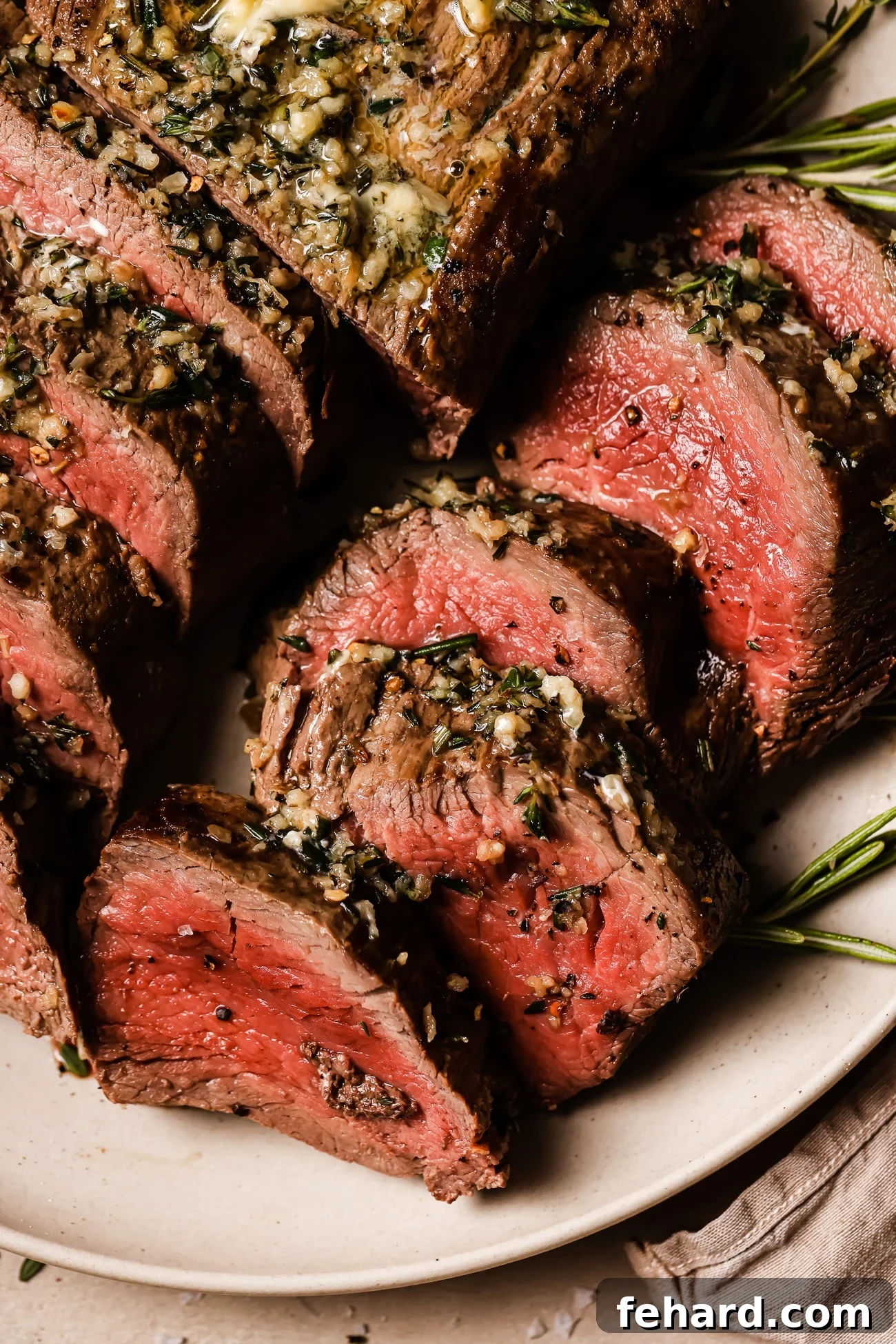 Golden Garlic Butter Tenderloin 10 A closeup of sliced beef tenderloin on a white serving plate.