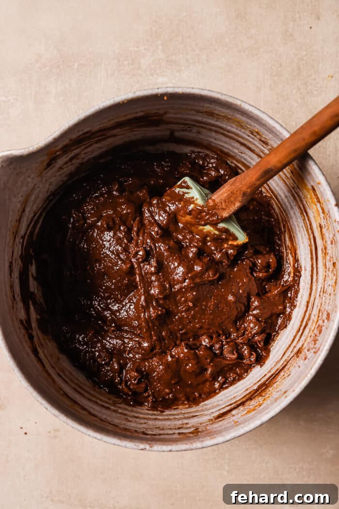 Eggs, maple syrup, and vanilla are added to the creamy pumpkin and peanut butter batter in a bowl.