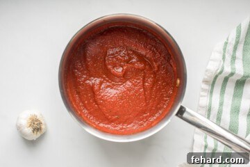 Perfect Pizza Sauce From Scratch 4 The pizza sauce gently simmering in a small saucepan, its color deepening and texture thickening as it cooks.