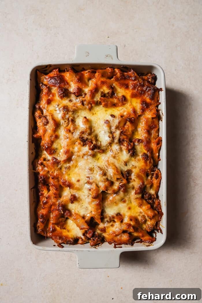 Baked ziti with ground beef in a white baking dish with melted cheese on top. 