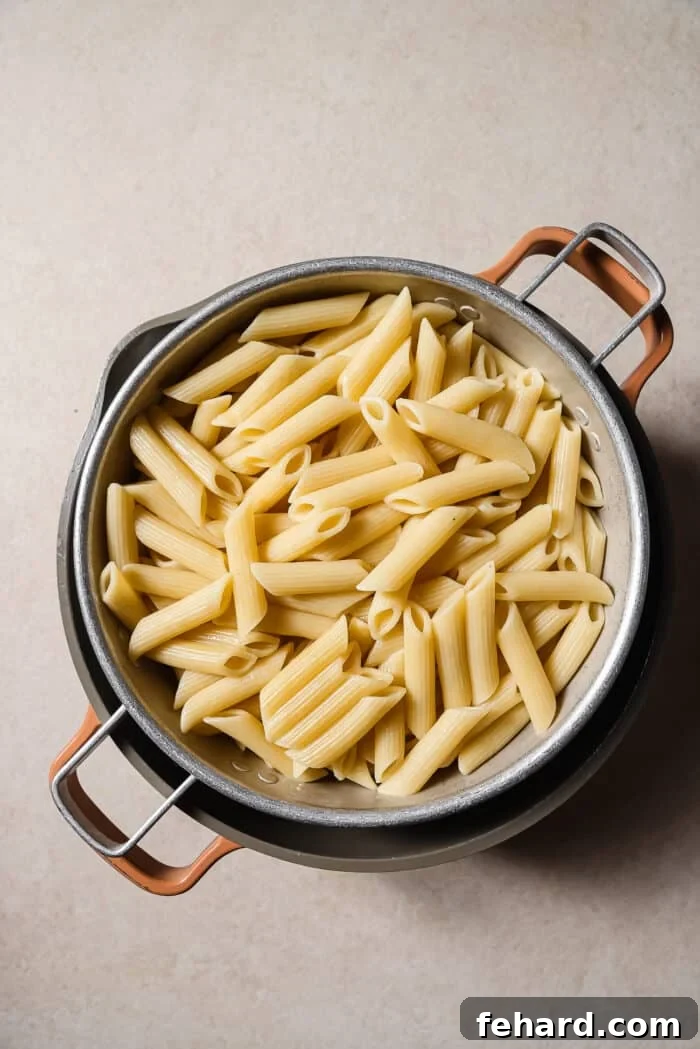 An overhead view of cooked penne pasta in a colander. 
