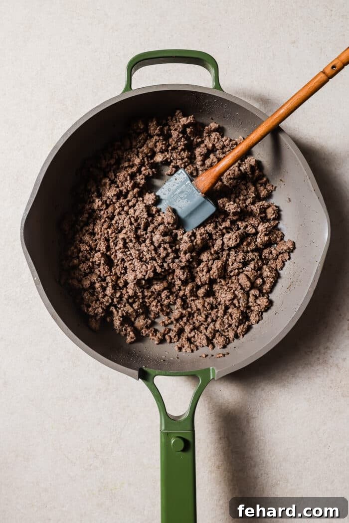 An overhead view of ground beef in a skillet with a wooden spoon in it. 