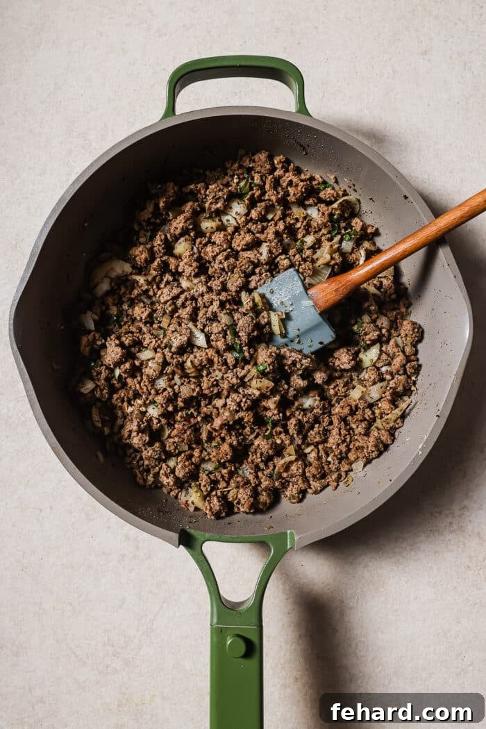 Onions, garlic, and seasonings are added to the skillet with the ground beef. 
