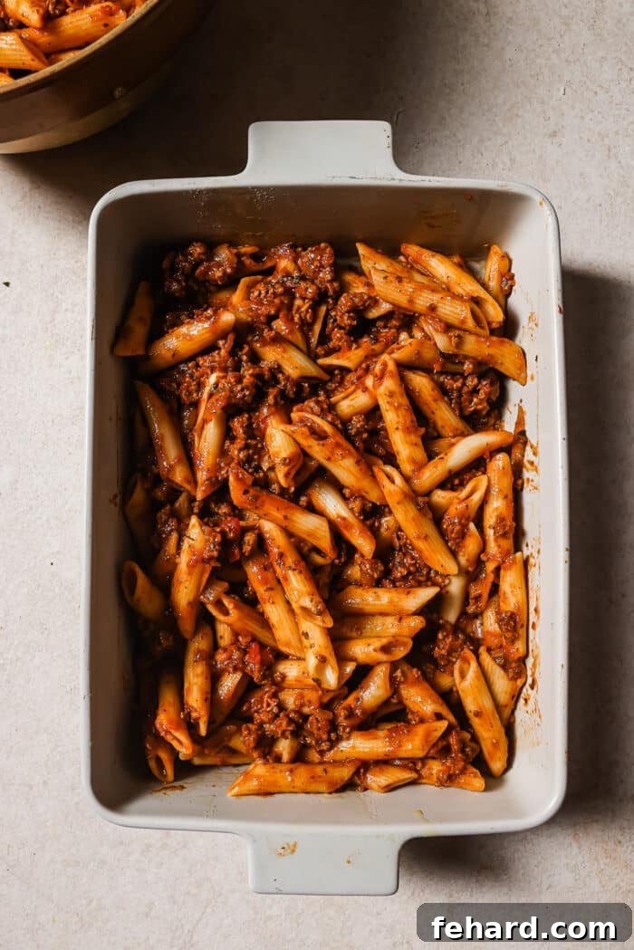 An overhead view of pasta and meat sauce combined in a white baking dish. 