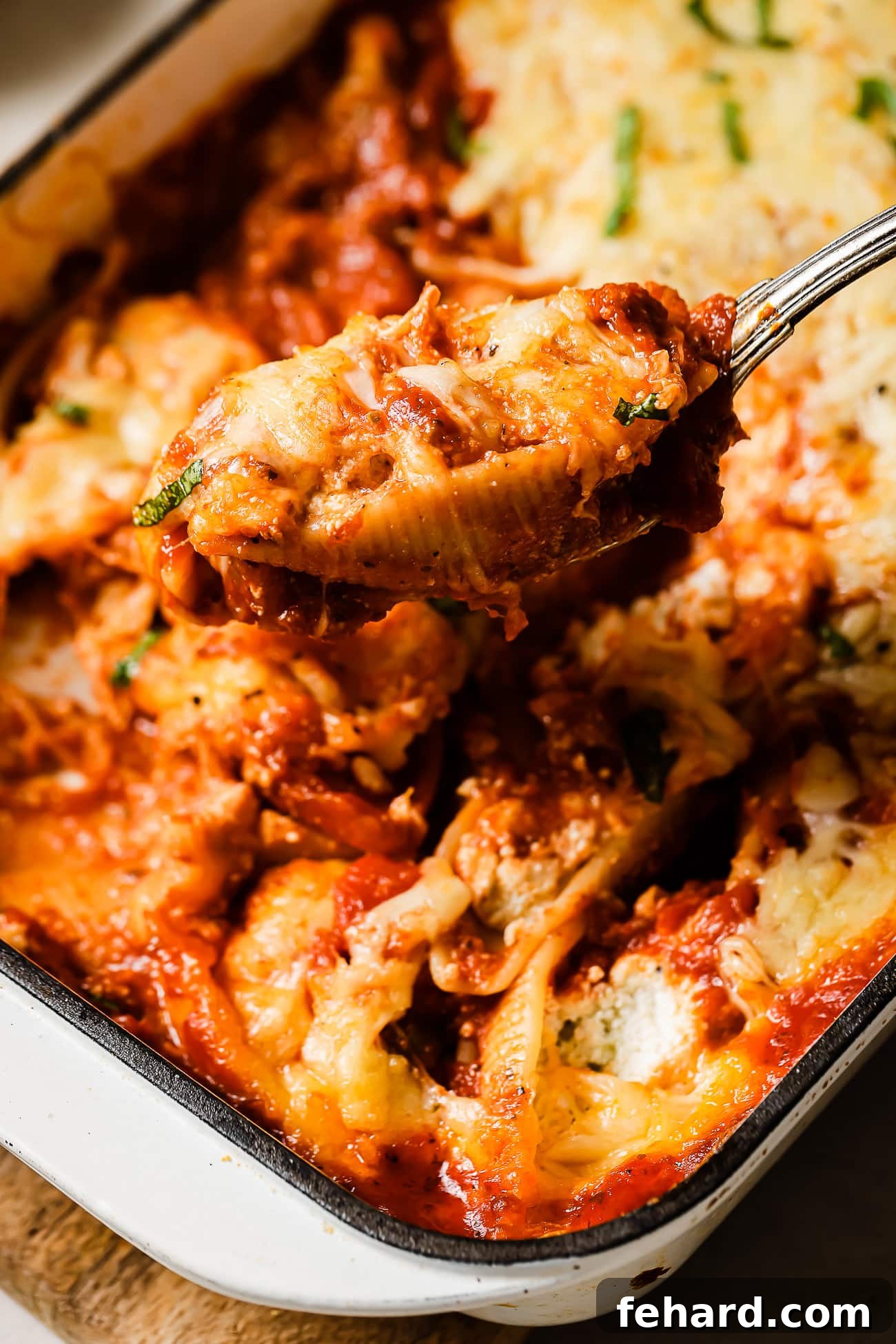 Stuffed shells in a white baking dish with a spoon removing a serving. 