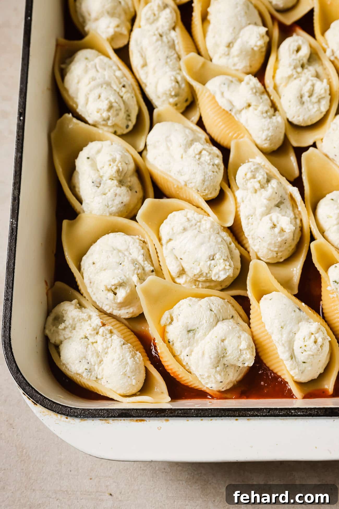 Giant shells stuffed with cheese in a white baking dish. 