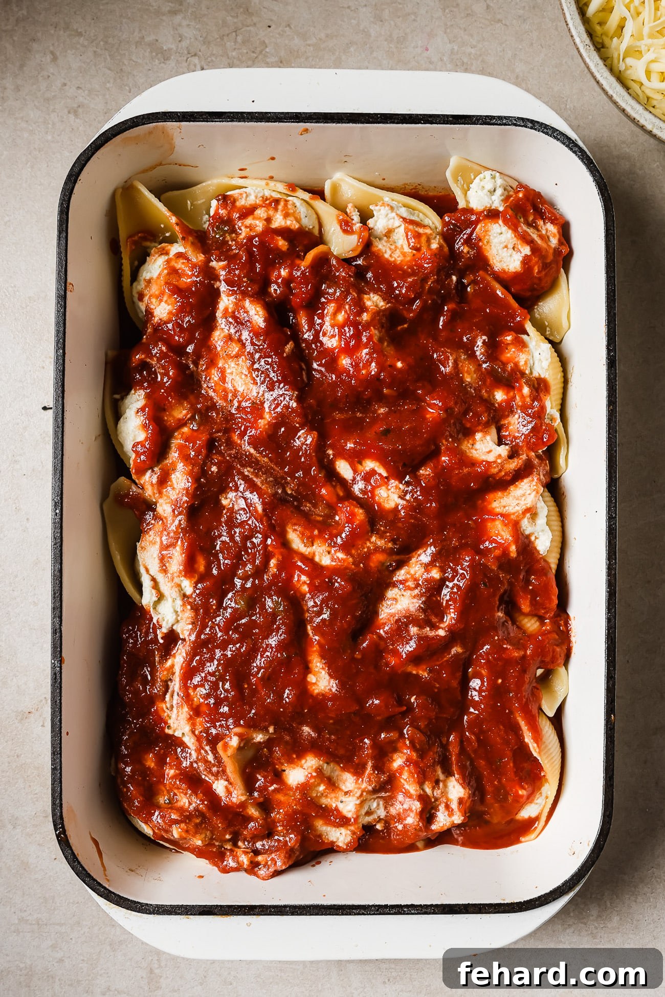 An overhead view of a baking dish with stuffed shells covered with marinara sauce. 