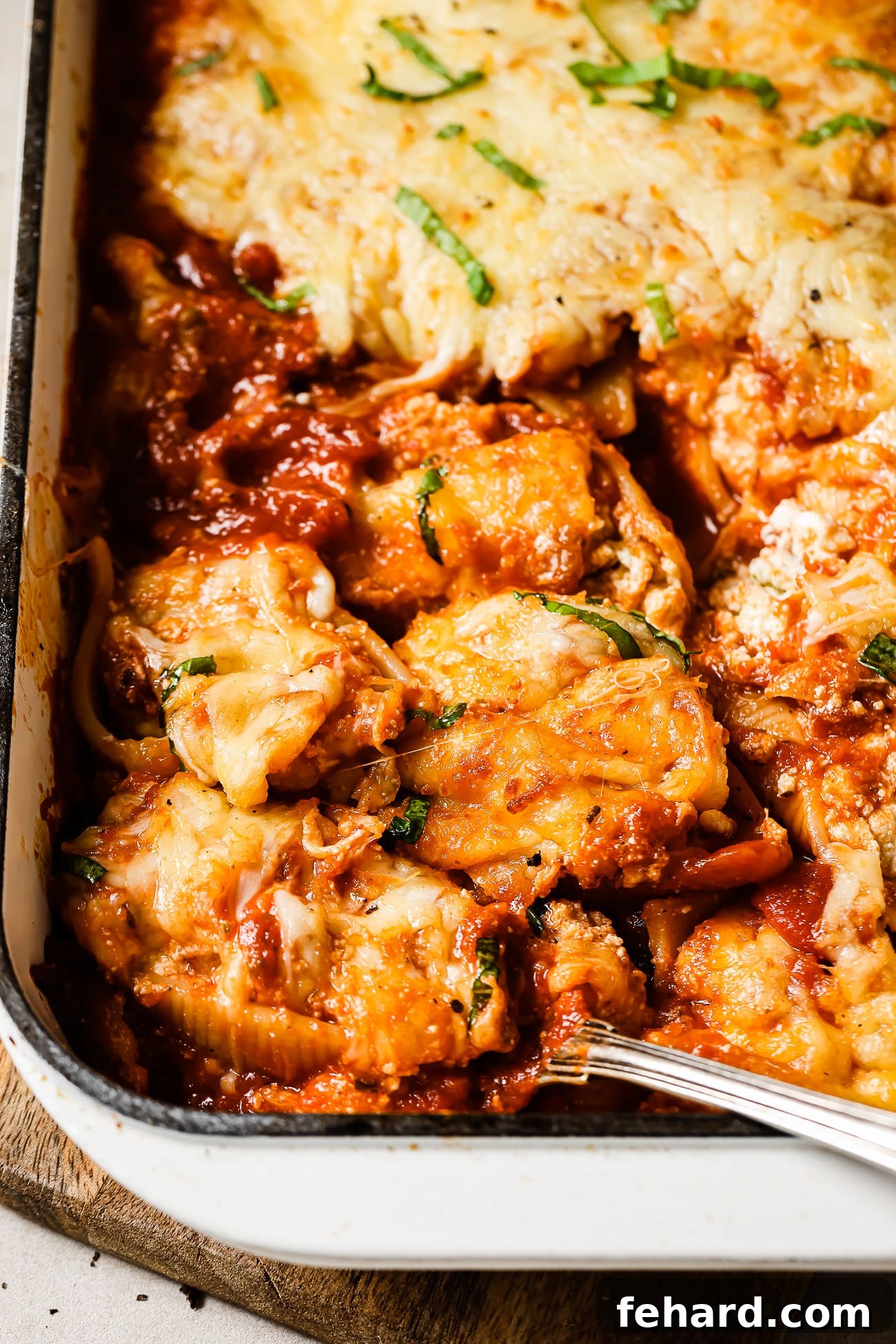 Stuffed shells in a white baking dish with a large spoon taking out a serving. 