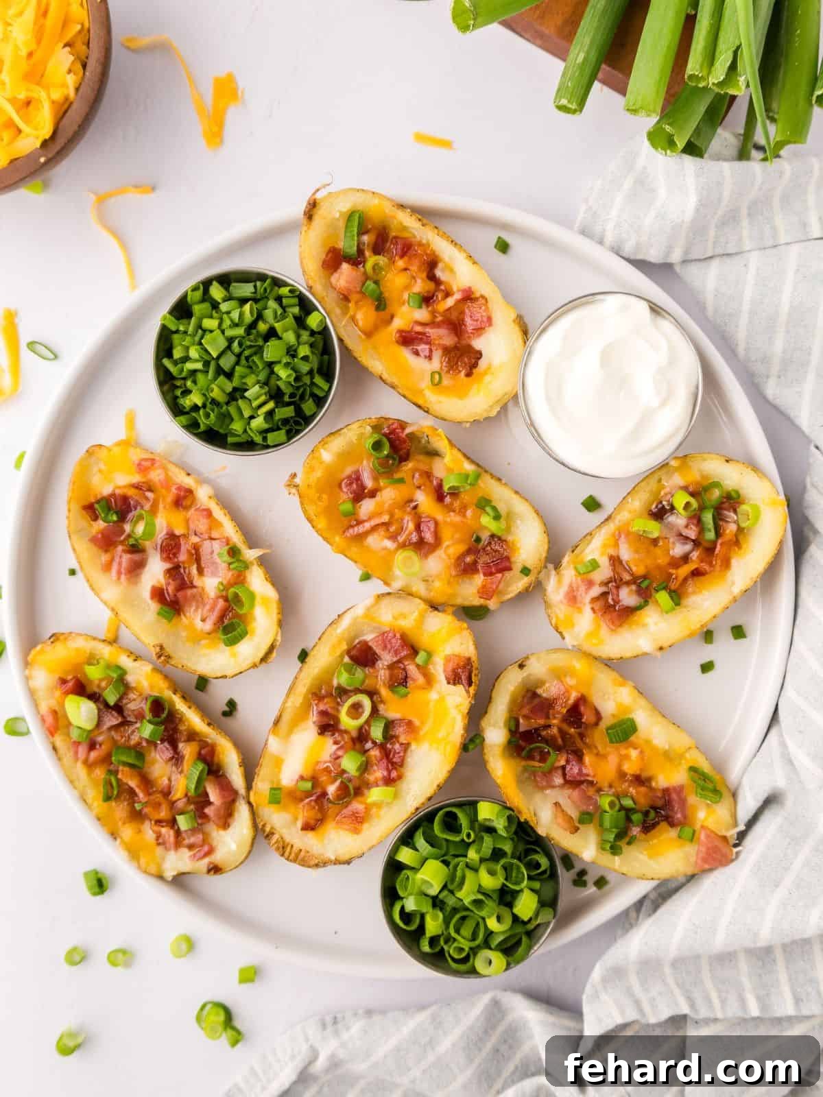 Loaded Potato Skins Loaded potato skins on white platter served with green onions and a dish of sour cream on the side.