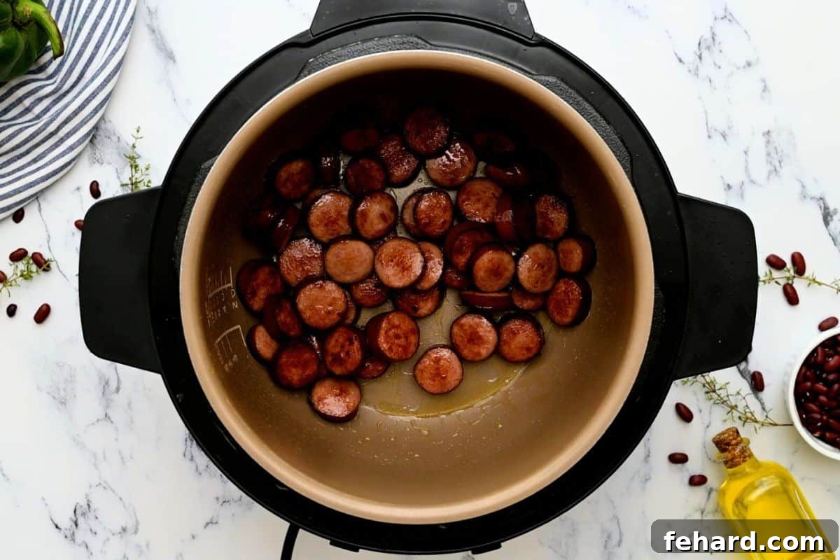Sliced andouille sausage sizzling and browning inside the inner pot of an Instant Pot.
