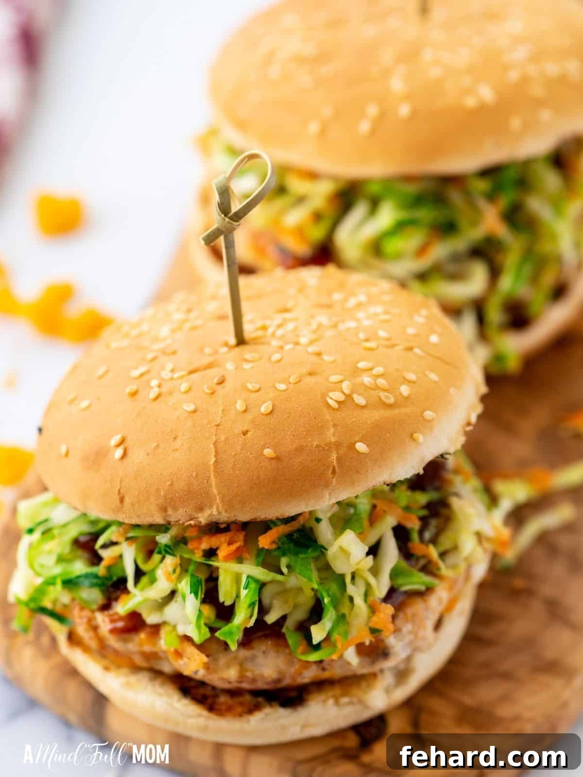 Two perfectly cooked BBQ chicken burgers topped with fresh coleslaw, resting on a rustic wooden cutting board.
