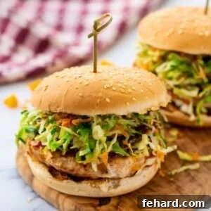 Juicy chicken burger on bun topped with BBQ sauce and coleslaw on cutting board.