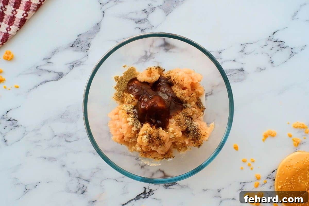 Raw ground chicken in a mixing bowl, lightly seasoned with spices, ready for cheese incorporation.