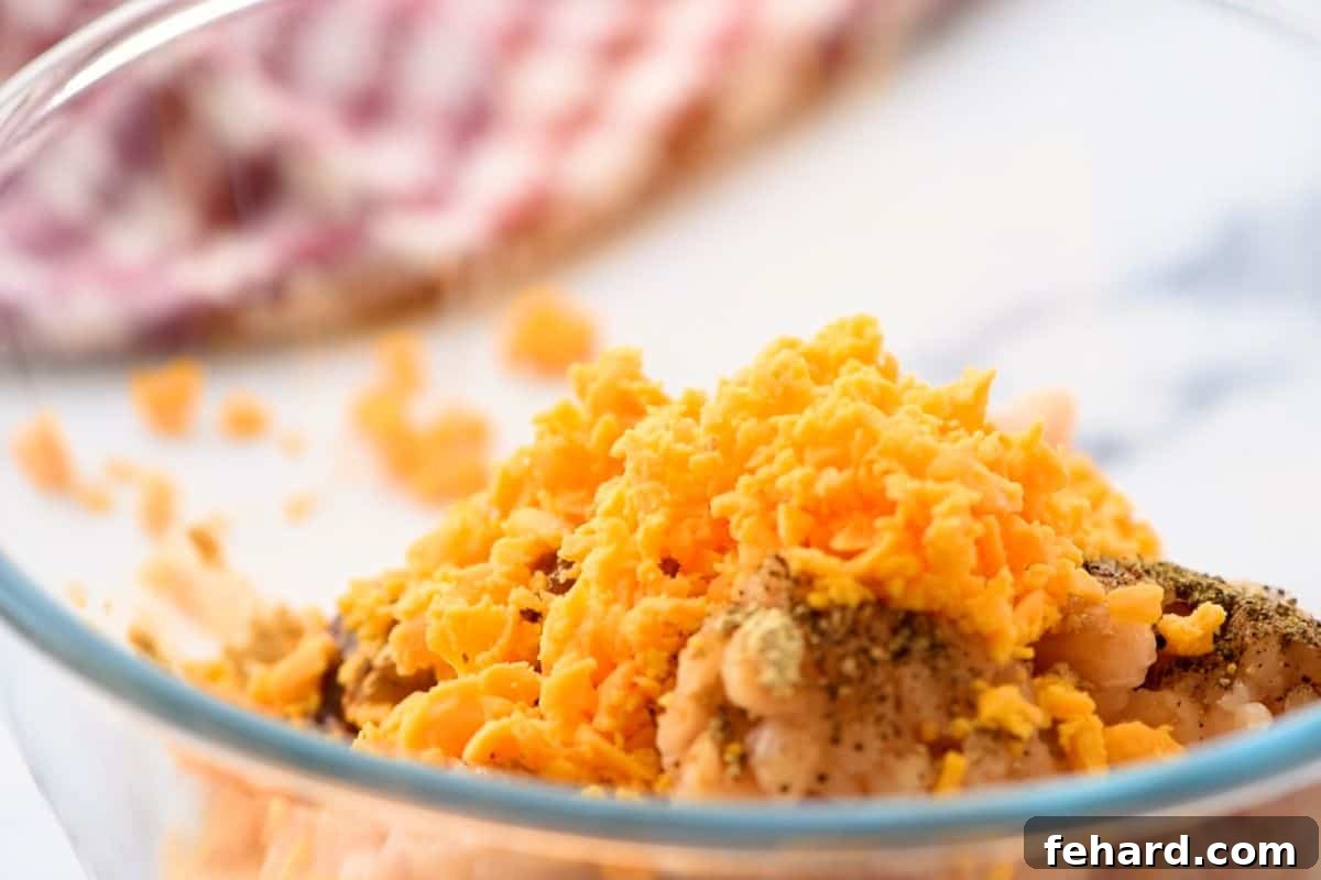 Diced sharp cheddar cheese being gently folded into the seasoned ground chicken mixture in a bowl.