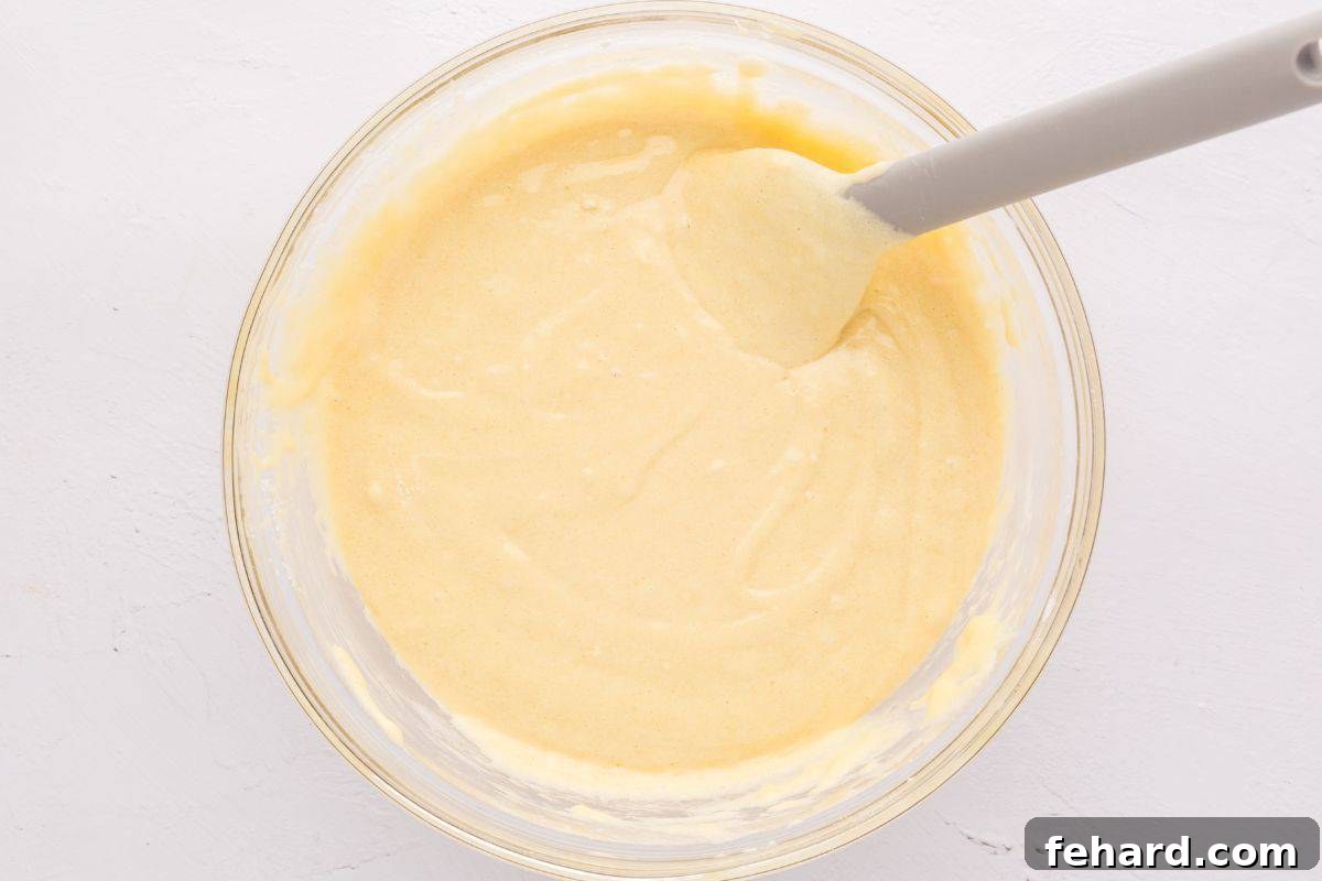 A mixing bowl containing the perfectly folded Hot Milk Cake batter, smooth and light in texture, with a spatula resting in the bowl.