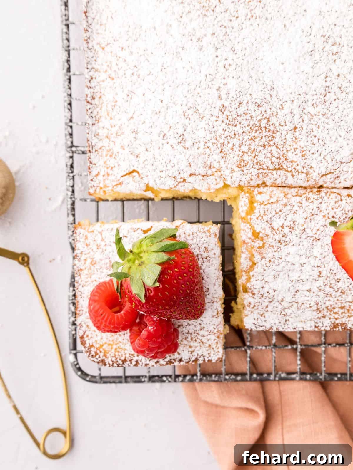 A whole Hot Milk Sponge Vanilla cake resting on a cooling rack, beautifully dusted with powdered sugar and garnished with fresh fruit, showcasing its inviting golden hue and light texture.