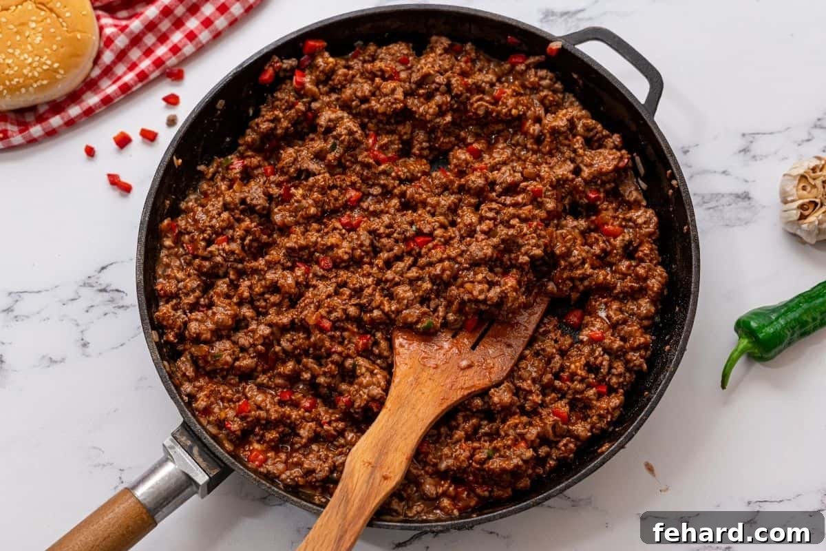 Skillet filled with homemade sloppy joes, surrounded by toasted buns and sliced jalapeños, ready for serving.