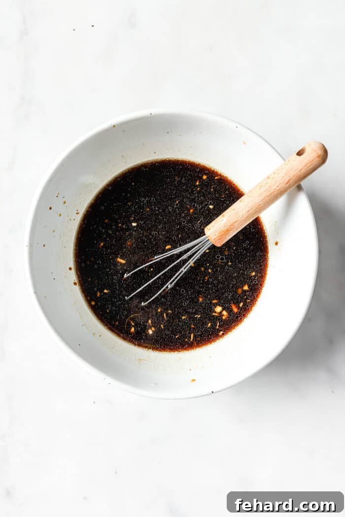 A white bowl full of dark sauce with a whisk in it. 