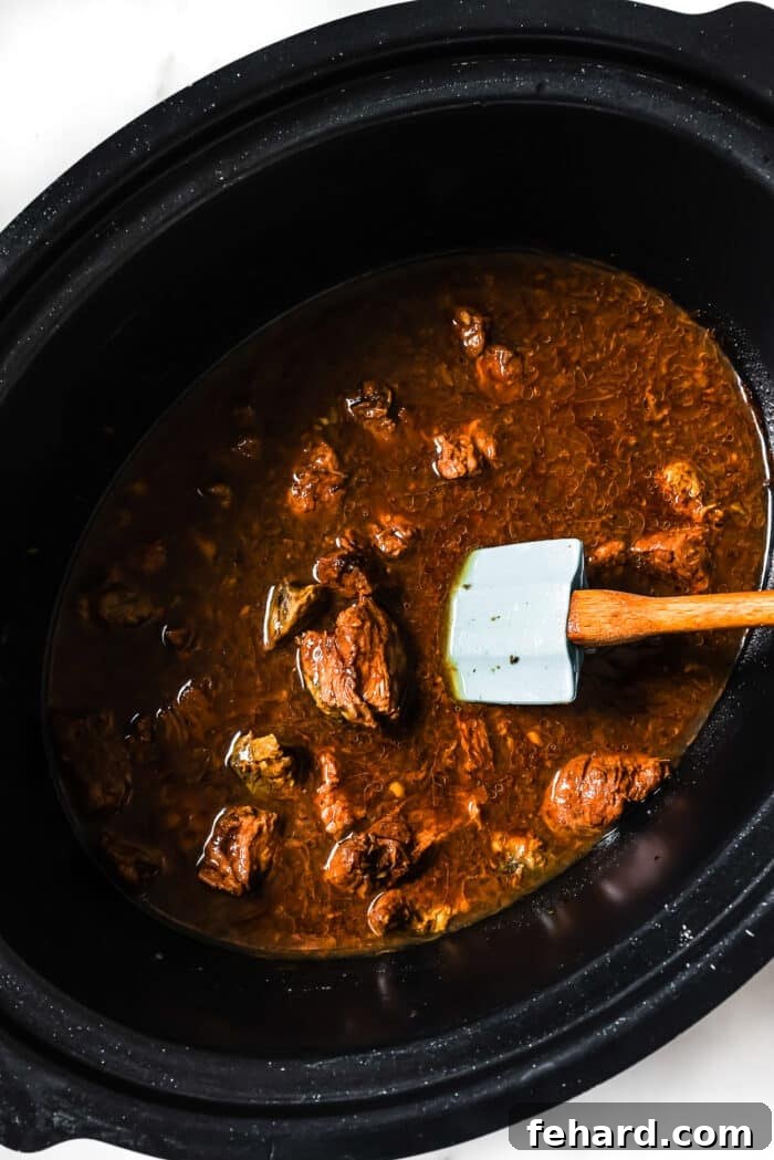 Slow cooker Korean beef in a black slow cooker with a blue spoon in it. 