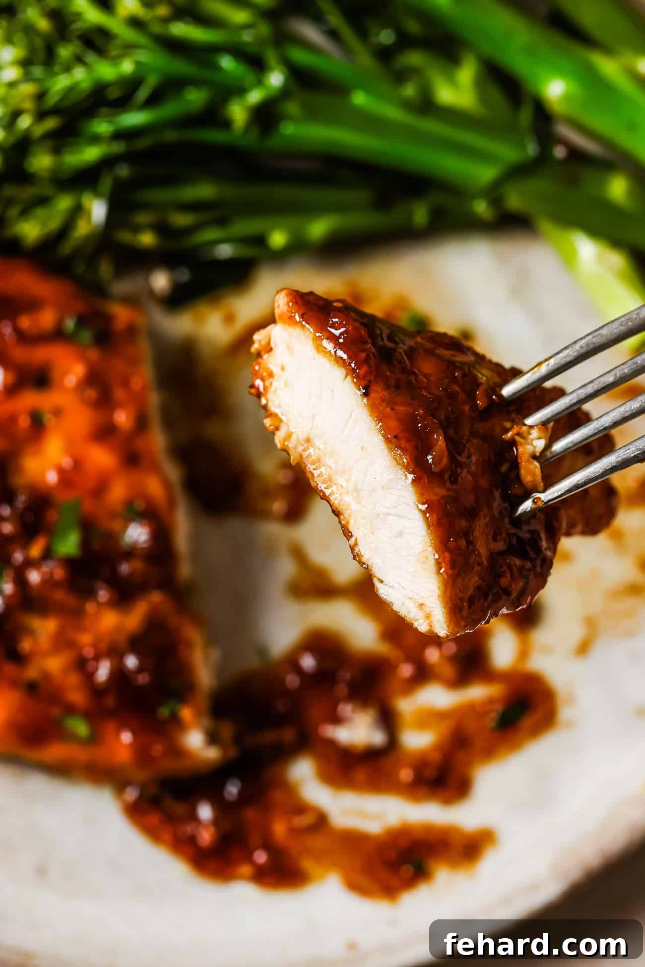Sticky Honey Garlic Chicken Breast 11 A close-up of a perfectly glazed piece of honey garlic chicken breast on the tip of a fork, highlighting its succulent and tender texture.