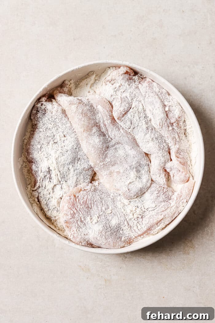 Sticky Honey Garlic Chicken Breast 4 A large white bowl full of chicken cutlets dredged evenly in flour, ready for searing in the skillet.