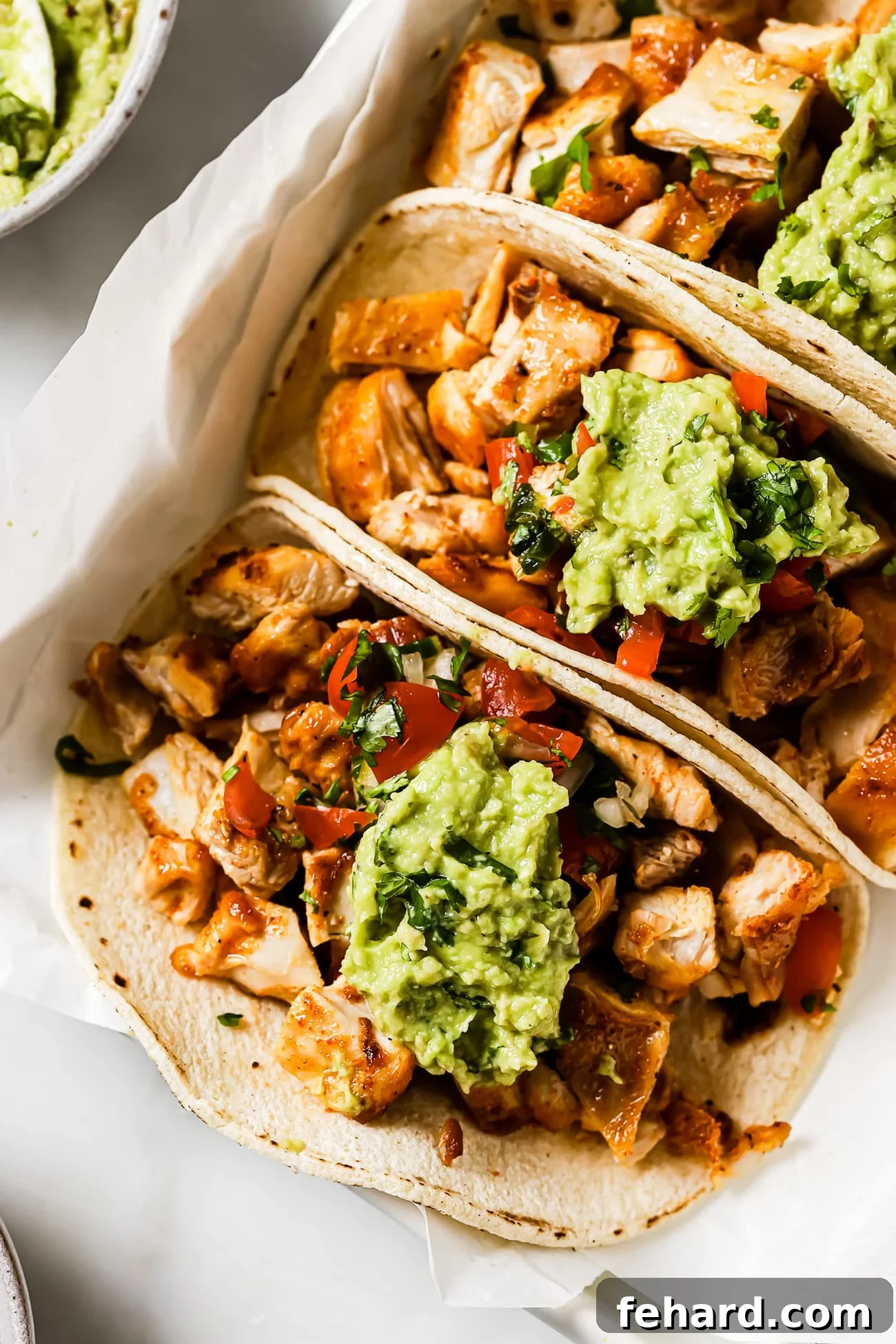 Flavor-Packed Homemade Chicken Tacos 10 Three chicken tacos topped with Pico de Gallo and guacamole on parchment paper.