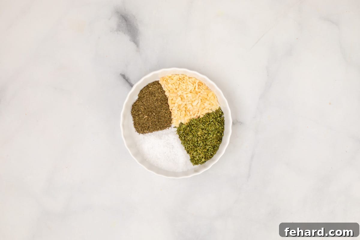 A collection of dried spices, including dill, parsley, onion flakes, and kosher salt, arranged in a white dish on a kitchen counter, ready to be blended into homemade dill seasoning.