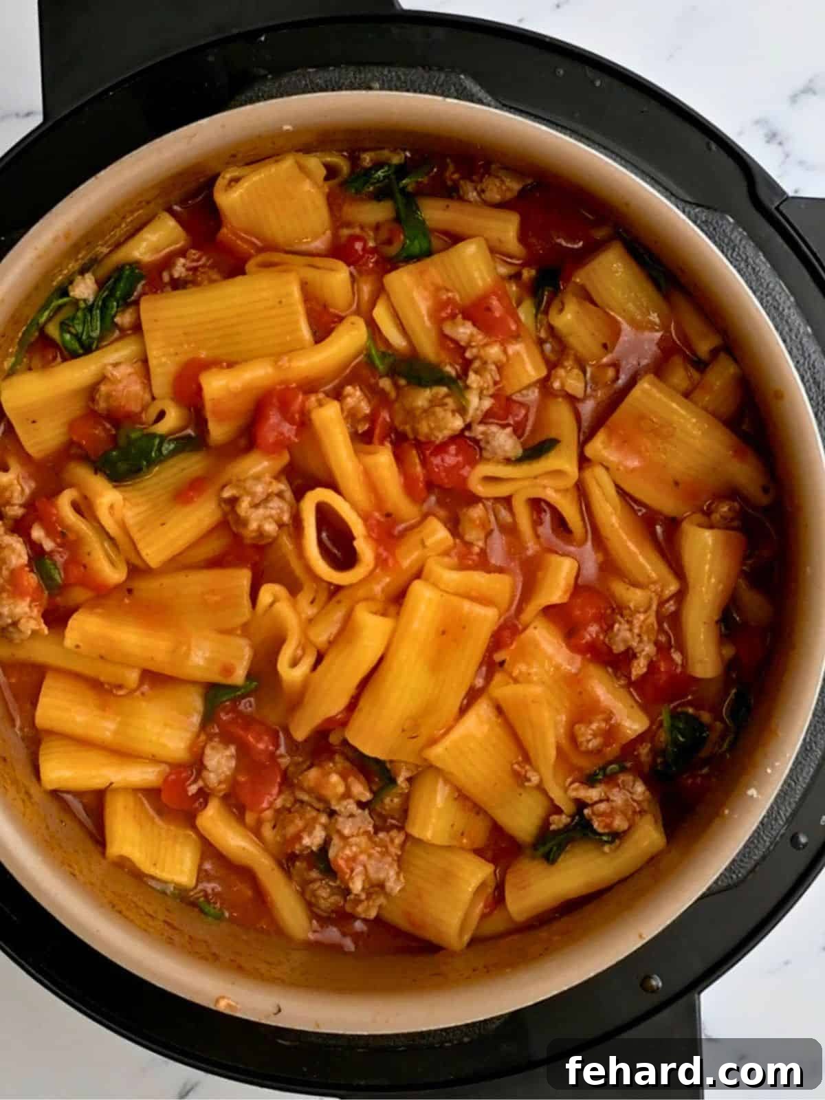 Instant Pot filled with perfectly cooked rigatoni and sausage in a diced tomato sauce, ready for spinach and cheese.