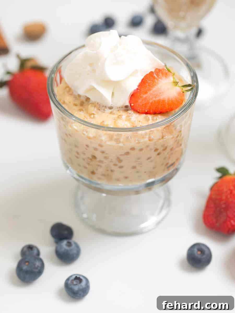 Tapioca Pudding Recipe Tapioca pudding in small serving bowl topped with fresh whipped cream and strawberries with berries in background.