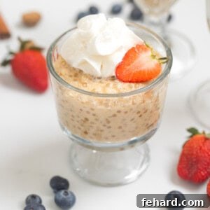Tapioca pudding in small serving bowls topped with fresh whipped cream and strawberries with berries and cinnamon sticks in background.