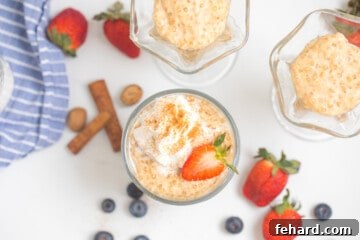 Tapioca pudding in small serving bowls topped with fresh whipped cream and strawberries with berries and cinnamon sticks in background.