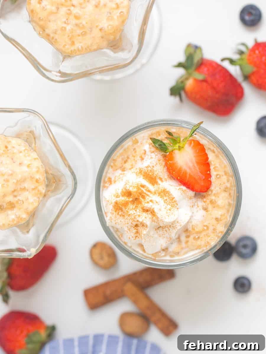Creamy Tapioca Pudding Recipe Tapioca pudding in small serving bowls topped with fresh whipped cream and strawberries with berries and cinnamon sticks in background.