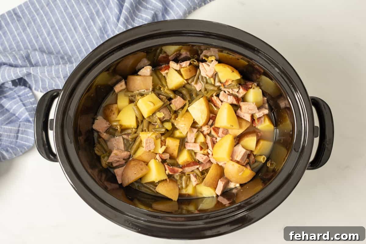 A slow cooker filled with the finished ham, green beans, and potatoes, all cooked to perfection and stirred together, ready to be served from the pot.