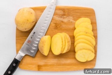 Yukon gold potatoes on wooden cutting board being cut into ¼-inch thick slices.